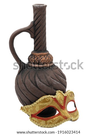 A traditional golden Venetian carnival mask next to an ornate clay wine bottle. The photo is isolated on a white background. The concept of the annual Brazilian festival.
