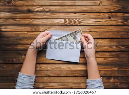 Dollar in an envelope in children's hands. Material aid, donation, alimony. Wooden grunge brown background.