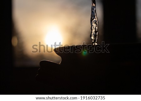 Silhouette water pour into clay vessel Royalty-Free Stock Photo #1916032735