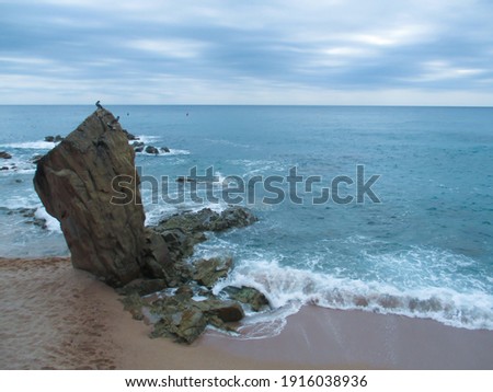 A large rock on the shores and a rough sea with waves.