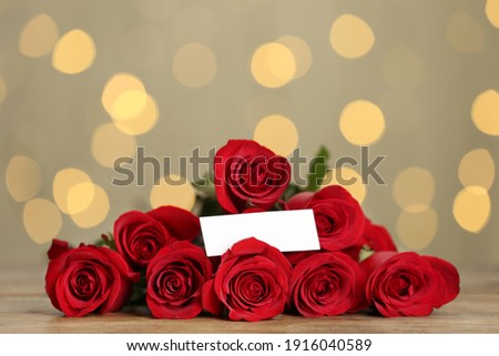 Beautiful red roses with blank card on table against blurred lights. St. Valentine's day celebration