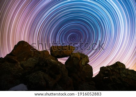 The rocks silhouette on the hill under the colorful star trails on the sky. Night timelapse photography.