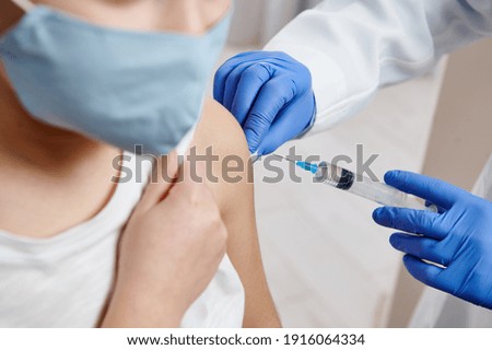 Closeup of hands wearing medical protective gloves holding syringe and making vaccine injection on a child arm Royalty-Free Stock Photo #1916064334