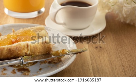 Table set with a quick continental breakfast with a cut croissant with spread orange marmalade, silver knife, on a white plate, fresh 
orange juice, espresso coffee in a white elegant cup. Close up.