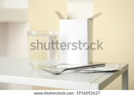 Medicine sachets, glass of water and spoon on white table