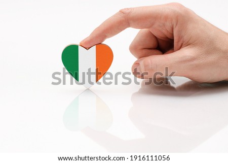 Love and respect Ireland. A man's hand holds a heart in the shape of the Ireland flag on a white glass surface. Irish patriotism and pride.
