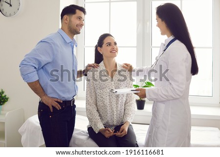 Happy married couple seeing family doctor. Clinician talking to young husband and wife. Patients listening to gynecologist at health center or hospital. Effective treatment, planning pregnancy concept Royalty-Free Stock Photo #1916116681