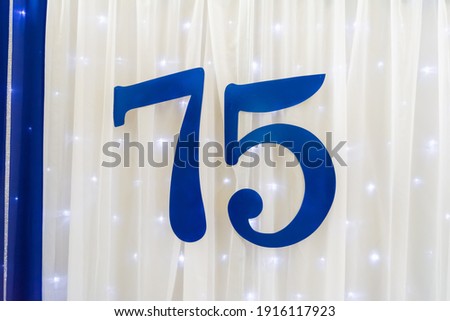 Blue inscription 75 on a background of white fabric and shimmering garland. Cover for the anniversary event