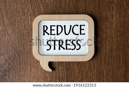A wooden plaque with the inscription REDUCE STRESS lies on the table. View from above. Flat lay. Marketing concept. Royalty-Free Stock Photo #1916122312