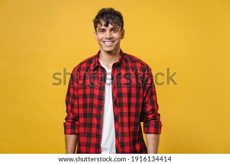 Young spanish latinos attractive handsome smiling cheerful stylish fashionable student man 20s wear red checkered shirt, white t-shirt look camera isolated on yellow color background studio portrait