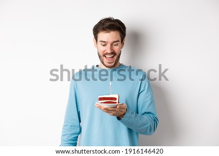 Cheerful man looking happy at birthday cake, celebrating bday, standing over white background