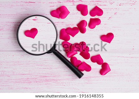 the heart lies under a magnifying glass, among many other hearts on a light wooden background. Love search concept. High quality photo