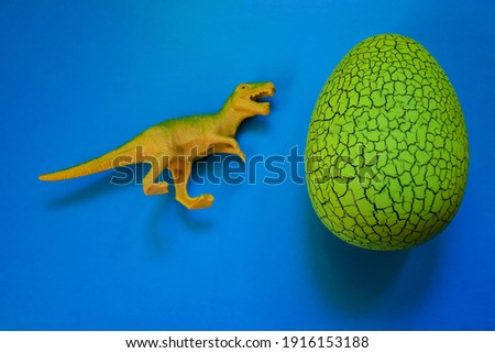 On a blue background, a huge yellow dinosaur egg with a dinosaur. Space for text, top view.
