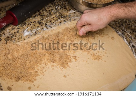 Man's hands sprinkling filling onto bread dough rolled out on granite countertop