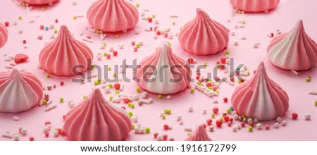 Pink and white pastel colored meringues with colorful sweet candy on pink pastel background. Happy birthday greeting card. Sweet candy concept. Banner.                           