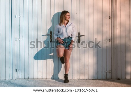 young blond girl in blue shorts passing in a white wood wall