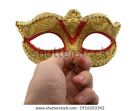 A man holds in his hand a traditional golden carnival Venetian mask with a red ornament on a black background. Preparation for the Brazilian Festival and Mardi Gras, fat Tuesday.