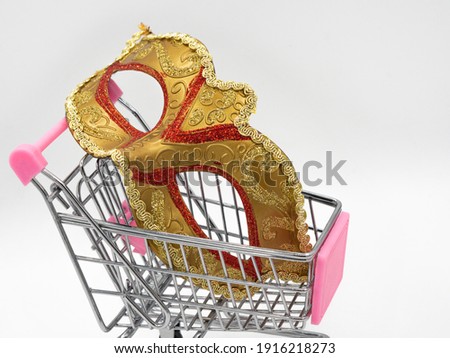 Traditional gold Venetian carnival mask toy mini shopping cart (trolley) on a white background. The concept of preparing for the annual Brazilian festival, buying costumes.