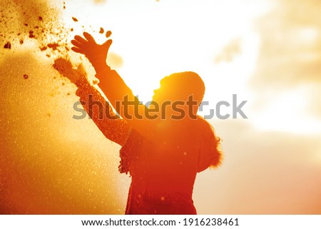 Silhouette of a woman among the snow in the backlight. The soul wants a holiday. A woman, illuminated by the winter yellow sun, throws snow in front of her. Playing with snow in the sun. 