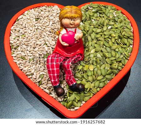 Girl holding a red heart in her arms. She is sitting on sunflower and pumpkins seeds. A good valentine day motive for a vegetarian. Love healthy food.