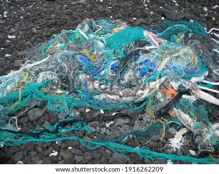 Tangled nets are found on a black rock beach. These nets while in the water pose a significant danger to marine life as, although lost and abandoned, they can continue ensnaring birds, turtles, fish