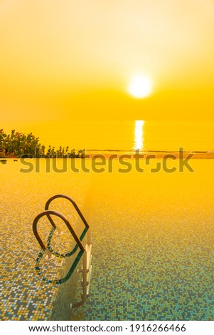 Outdoor swimming pool with sea ocean beach at sunset or sunrise time for leisure vacation