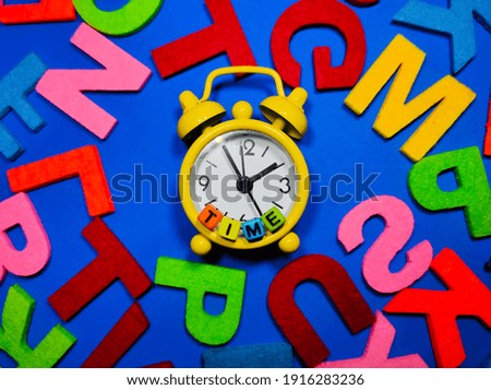 Selective focus.Alarm clock with word TIME and colorful word on blue background.Shot were noise and film grain.