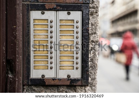 An intercom with blank name tags built into the entrance of a building on a busy urban street