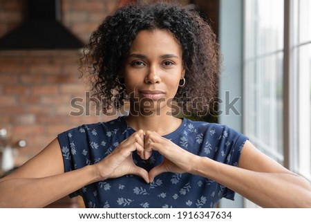 Head shot portrait close up grateful African American woman showing heart sign gesture, looking at camera, expressing love and care, female volunteer supporting, regular medical checkup promotion