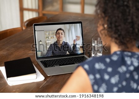 Back view close up African American woman making video call to Indian colleague, using laptop and webcam, diverse workers or friends chatting online, involved in conference, consulting client Royalty-Free Stock Photo #1916348198
