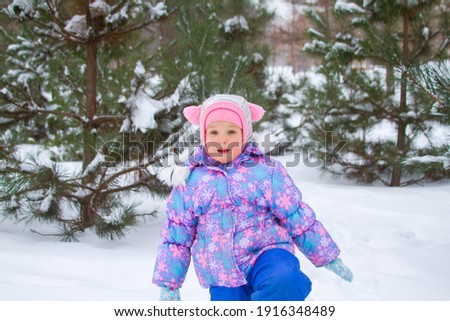 A cute girl in a winter overalls walks in the park in winter, a child walks through snowdrifts.

