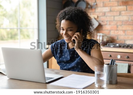 Close up happy African American woman making phone call, looking at laptop screen, talking, smiling friendly businesswoman reading information, consulting client or negotiating project with colleague Royalty-Free Stock Photo #1916350301