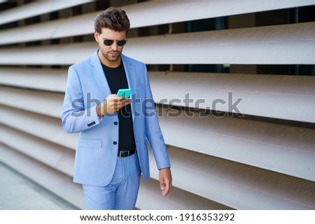 Young man walking down the street using his smartphone with a serious expression