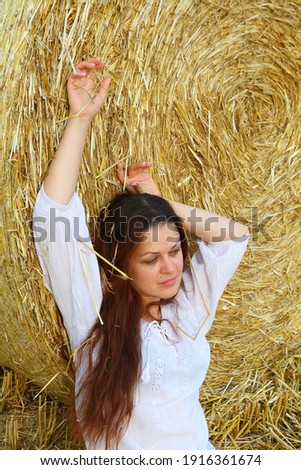 Girl in a white dress near a haystack in a field