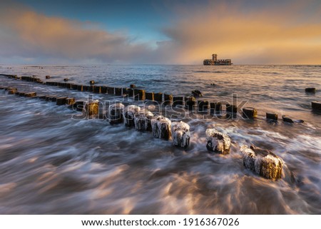 Winter landscape at the sea. Frozen wooden breakwaters line to the world war II torpedo platform at Baltic Sea. Morning at Babie Doly, Poland. Long exposure photo. Beautiful sunrise.