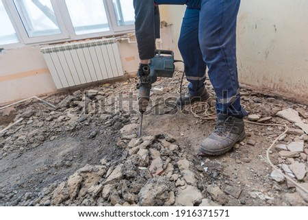 Working process of dismantling and disassembling the floor with construction electric perforator in room of apartment is that under construction, remodeling, renovation, extension, restoration and Royalty-Free Stock Photo #1916371571