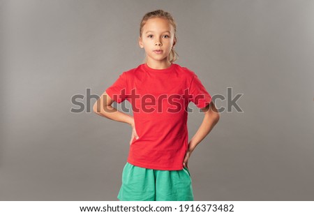 Cute girl in red shirt standing against gray background