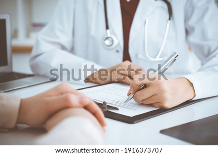 Unknown woman-doctor filling up an application form while consulting patient. Medicine concept Royalty-Free Stock Photo #1916373707