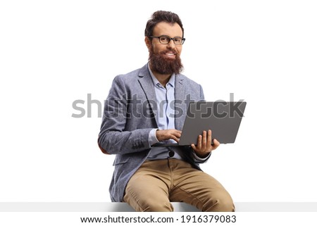 Bearded man seated on a blank panel with a laptop isolated on white background