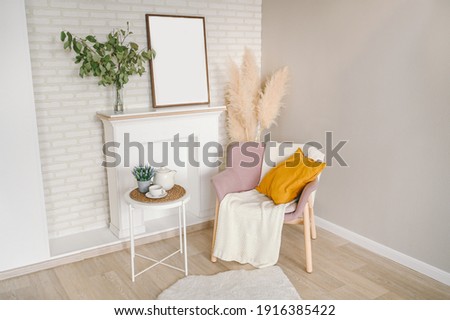 Breakfast still life scene. Coffee cup teapot white table, empty picture frame mockup, cozy stylish armchair blanket. Elegant working space, home office concept. Scandinavian interior room design