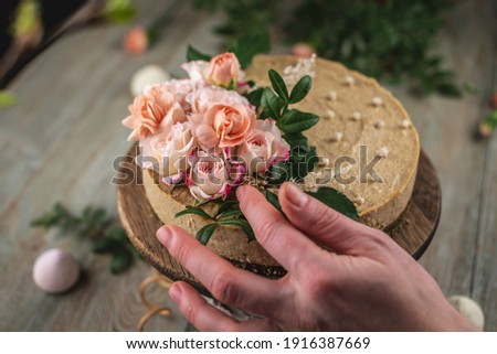 Decorator's hand is decorating the delicious raw mousse cake with tenderness pink flowers. Concept of romantic mood and spring atmosphere.