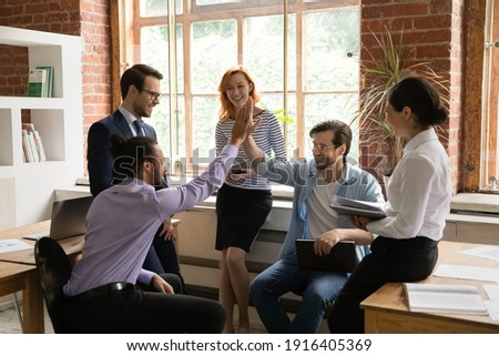 Overjoyed multiethnic male employees give high five motivated shared work success or promotion at meeting. Smiling multiracial men colleagues celebrate good job results engaged in office briefing. Royalty-Free Stock Photo #1916405369