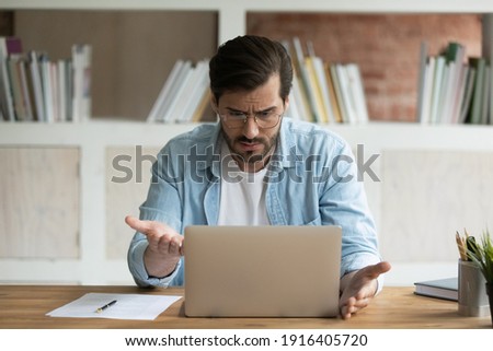 Unhappy Caucasian male employee work online on laptop in office frustrated by error or mistake on gadget. Upset mad man worker look at computer screen confused by slow internet or device breakdown. Royalty-Free Stock Photo #1916405720