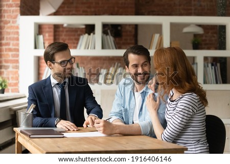 Happy Caucasian young couple clients consult with realtor or broker sign contract make agreement in office. Excited man and woman spouses feel overjoyed closing deal with real estate agent at meeting. Royalty-Free Stock Photo #1916406146