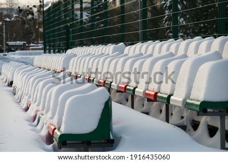 Raws of outdoor stadium seats heavily covered with snow "caps" in winter. Selective focus.