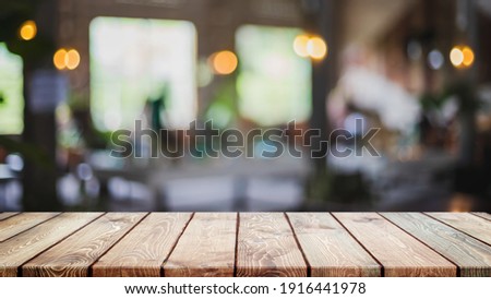 Empty wood table top and blurred coffee shop, cafe and restaurant interior background - can used for display or montage your products. Royalty-Free Stock Photo #1916441978