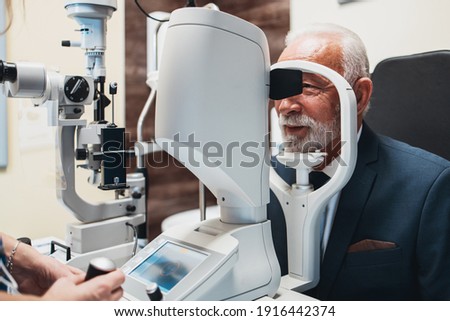 Elegant senior bearded man receiving ophthalmology treatment. Doctor ophthalmologist checking his eyesight with modern equipment. Royalty-Free Stock Photo #1916442374