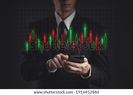 Businessman in black suit using smartphone planning for investment. Showing candlestick chart hologram technology.
