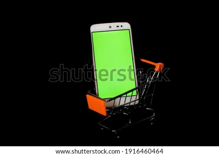Smartphone in small shopping trolley or cart. The phone screen is green. Online shopping concept. Black background.