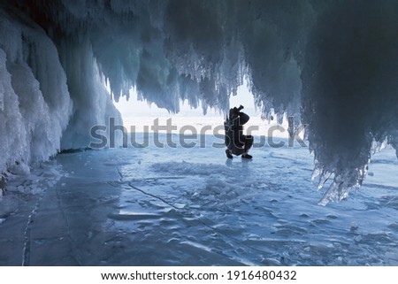 Frozen Baikal Lake. View from the ice-covered grotto Olkhon Islands on the silhouette of a tourist with a camera. Winter unusual photo travel
